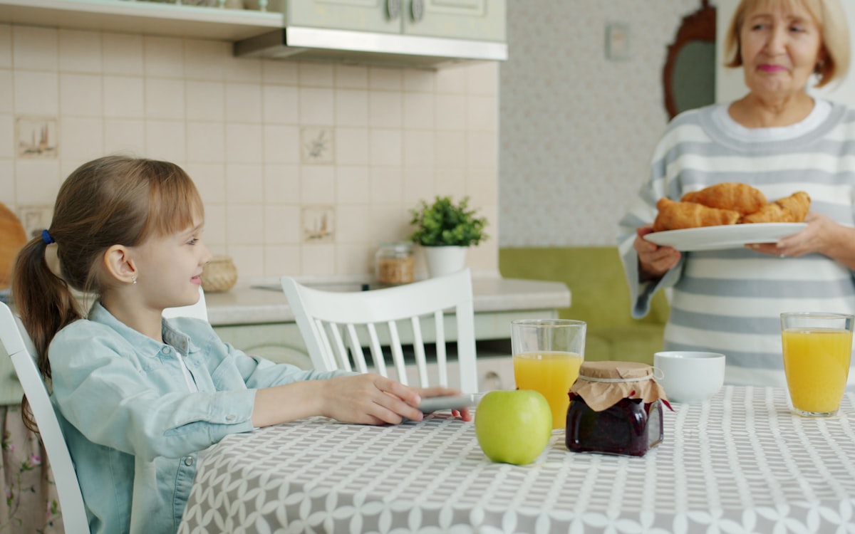 Grandmother serves croissants to girl at kitchen table