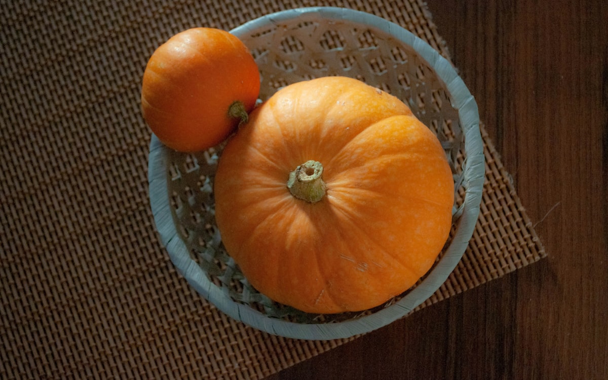 Two pumpkins in a decorative bowl on a wooden surface